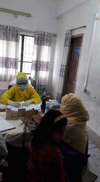 孟加拉国的一名医生在看病间隙穿着全套个人防护装备(PPE)。医生身后的婴儿床是因为在COVID-19大流行期间，由于医生短缺，他们需要长时间轮班。Photo by Aster Azalea