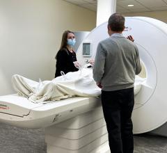 奥兰多·西蒙尼蒂(右)与核磁共振技术专家希瑟·赫米勒一起操作他帮助开发的一种新的经fda批准的核磁共振机器。该机器具有更低的磁场和更大的患者开口，扩大了以前无法进行MRI检查的患者的使用范围。